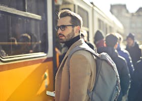 Man in Brown Coat and Gray Backpack Posing for a Photo